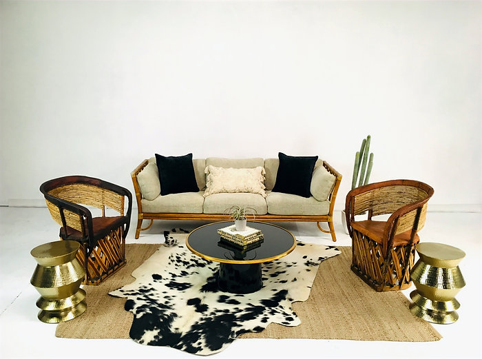 Woven rattan sofa with black and cream pillows, matching chairs, and brass drum side tables in a bright airy space