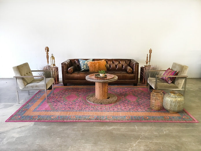 Brown leather tufted sofa with gray velvet armchairs and a round wood spool table in a warm inviting lounge arrangement