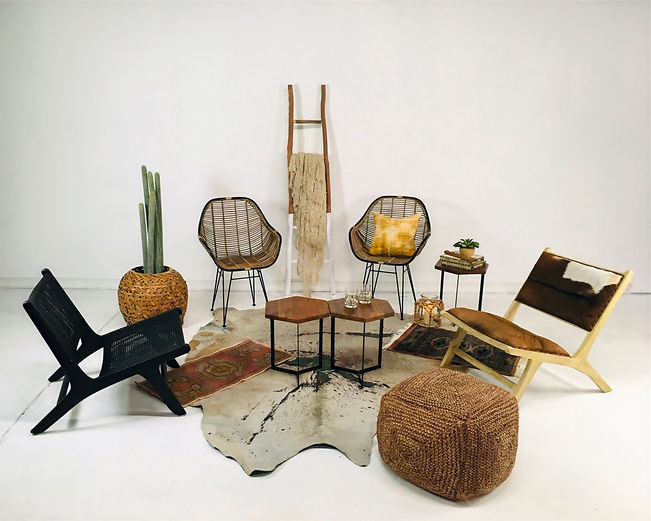 Varied lounge chairs, wicker seating, a cowhide rug, small wood tables, and a ladder decor piece in an eclectic arrangement