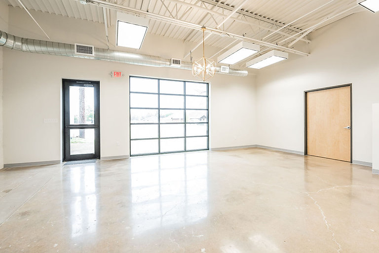 Empty room with polished concrete floor, white walls, exposed ceiling ductwork and a large window, lit in soft neutral tones, awaiting staged event decor