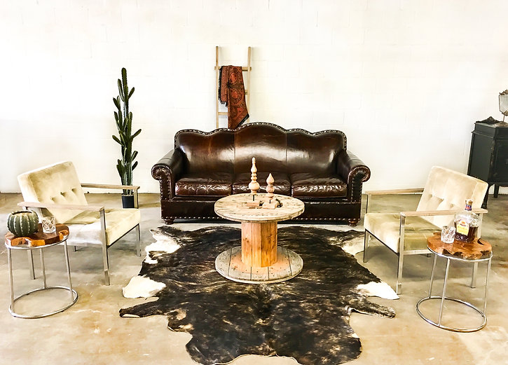 Brown leather tufted sofa with cream armchairs, round wood spool coffee table, and side tables in a cozy lounge