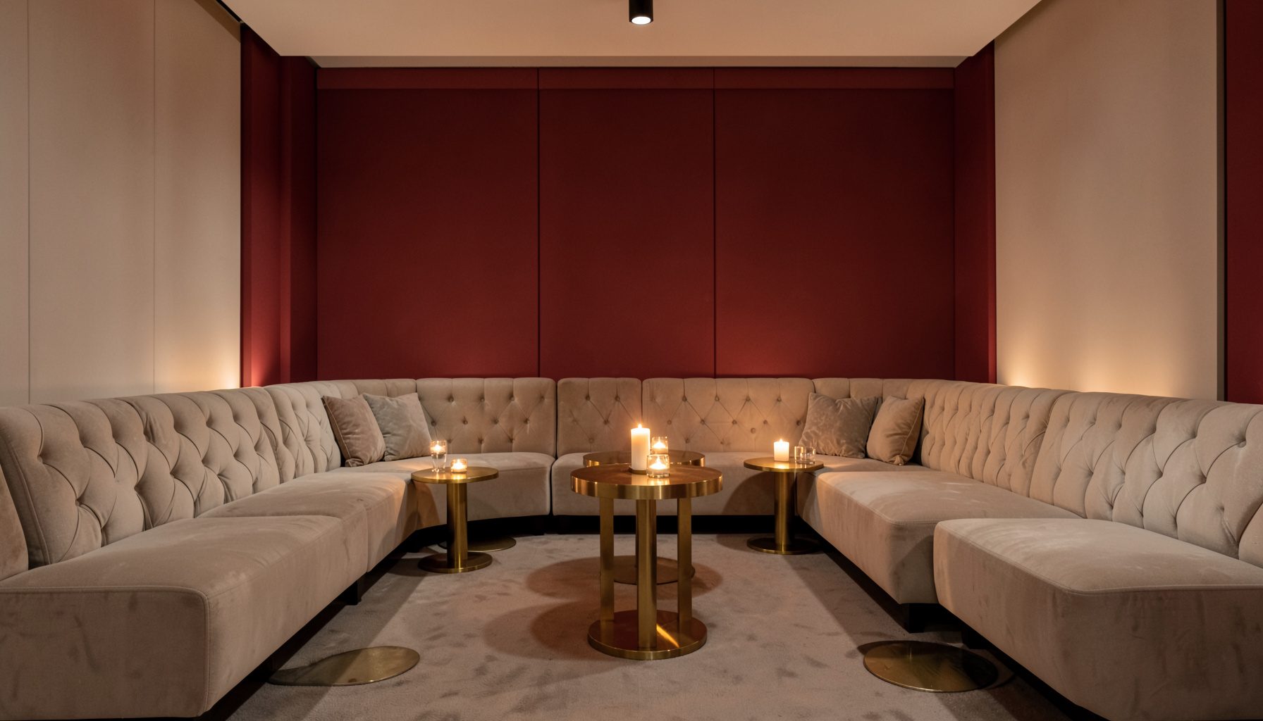 A softly lit event lounge with tufted beige settees, gold accent tables, and warm candlelight against a neutral backdrop.