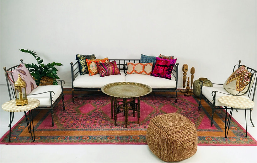 Bohemian-style seating area with a white cushioned daybed, colorful patterned pillows, wrought iron side tables, and a round rug