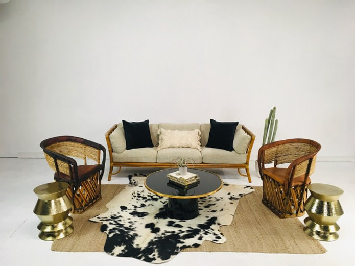 Woven rattan sofa with black and cream pillows, matching rattan chairs, and brass drum side tables on a patterned rug
