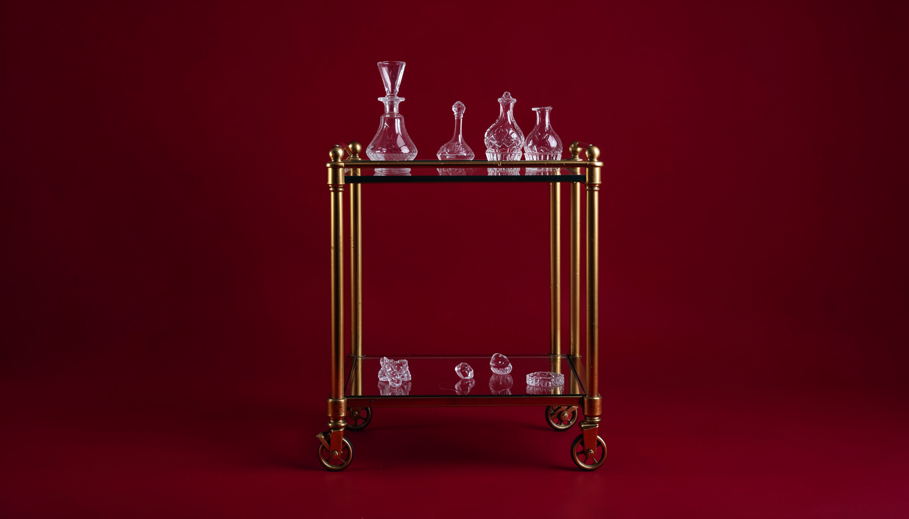 A vintage-style bar cart with brass wheels, glass shelves, and crystal decanters on top.